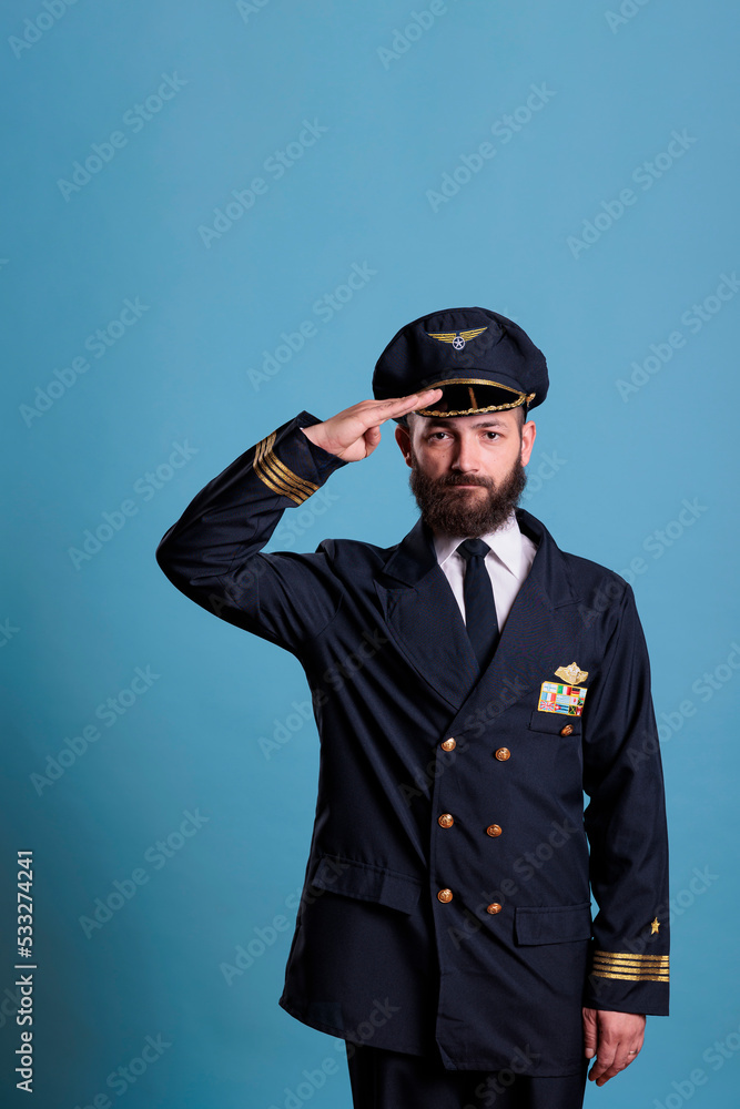 Confident airplane aviator saluting, wearing uniform and hat front view portrait, plane captain looking at camera. Civil captain with aircraft wings badge on jacket, professional aircrew member Confident airplane aviator saluting, wearing uniform and hat front view portrait, plane captain looking at camera. Civil captain with aircraft wings badge on jacket, professional aircrew member