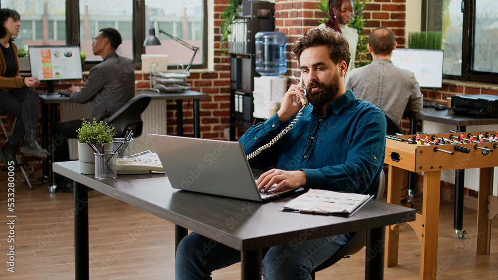 Project manager answering landline phone call in startup office, talking to employee on phone line. Using office telephone with cord to chat and have remote communication at job. Project manager answering landline phone call in startup office, talking to employee on phone line. Using office telephone with cord to chat and have remote communication at job.