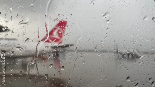 The view from the rain-splattered window of the plane and the take-off field. Raindrops fall on the glass and flow down. Rain outside the window. Bad weather in the city.