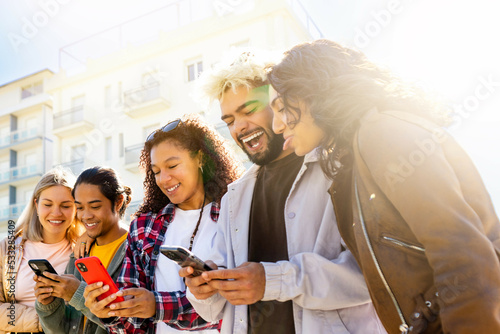 Happy Multiracial Group look at the phone smiling - multi ethinic group of young people laugh.   Student friends of various races laughing online social . Friends Concpet  photo