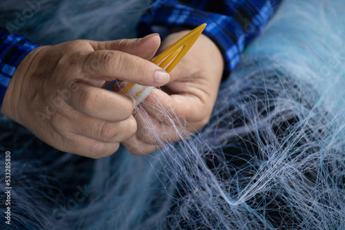 A Vietnamese woman in traditional clothes repairs a fishing net using a nylon thread. Close up of her hands and tool.