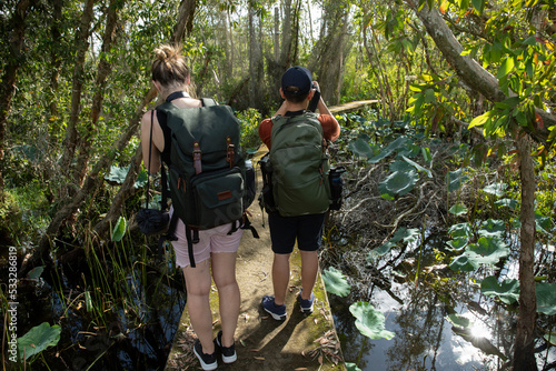 Young Male and female photographer from back view enjoying hiking in a tropical forest taking photos of landscape.