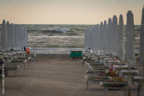 Fototapeta Naklejka Na Ścianę i Meble -  Big waves roll up on the beach. close parasol in bright Sunny day. White foaming waves and splashes.A hot summer day and high wave, seascape.Italy