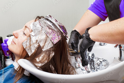 The hairdresser in black gloves paints a brunette woman's hair in the beauty salon.