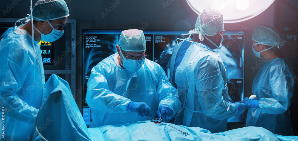 Diverse team of professional medical surgeons perform surgery in the operating room using high-tech equipment. Doctors work to save a patient in a modern hospital. Medicine, technology and healthcare. Diverse team of professional medical surgeons perform surgery in the operating room using high-tech equipment. Doctors work to save a patient in a modern hospital. Medicine, technology and healthcare.