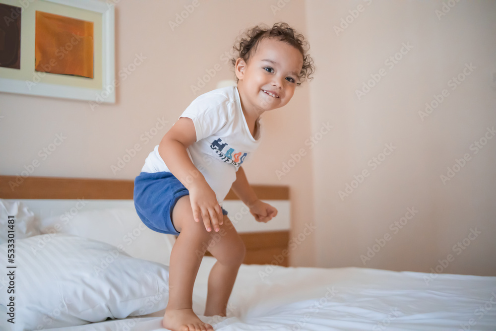 Curly toddler boy jumping and having fun on the bed Curly toddler boy jumping and having fun on the bed