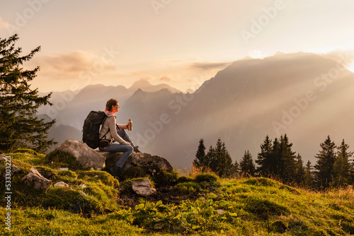 Woman with water bottle sitting on rock at sunset photo