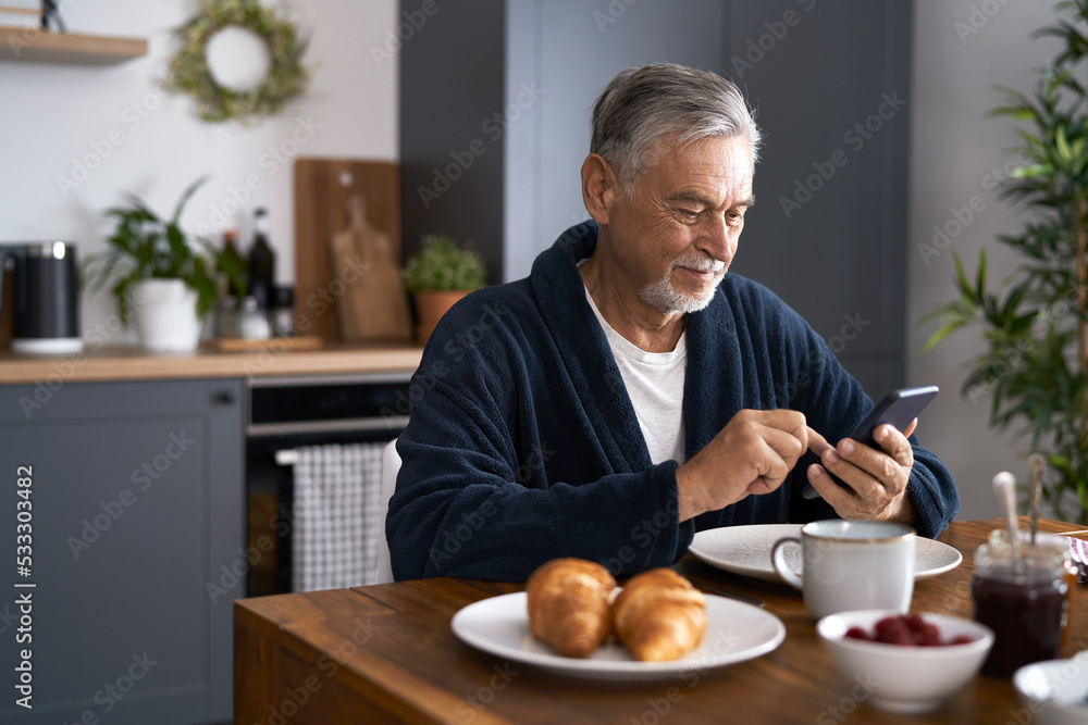 Senior caucasian man using mobile phone and eating breakfast Senior caucasian man using mobile phone and eating breakfast