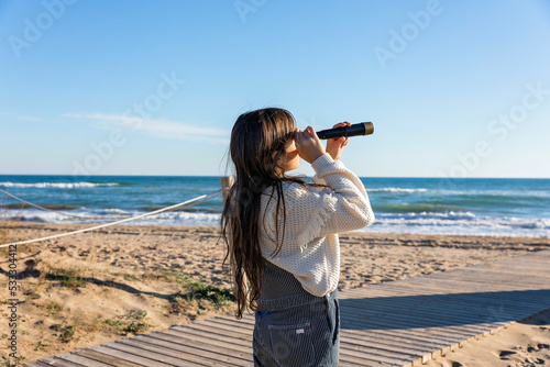 Girl watching sea through monocular on sunny day photo