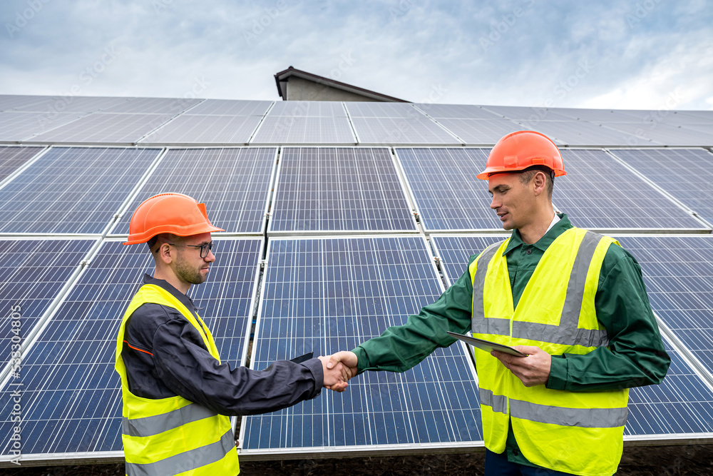 two workers in overalls and helmets shake hands after completing a panel plan. two workers in overalls and helmets shake hands after completing a panel plan.