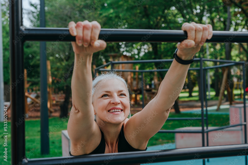 Happy mature woman stretching on bars in playground Happy mature woman stretching on bars in playground