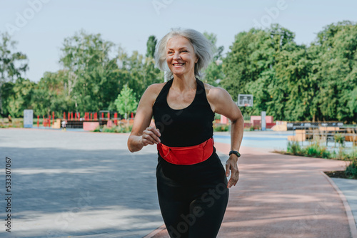 Happy mature woman with waistband jogging in park