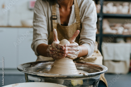 Hands of craftswoman molding clay on pottery wheel at workshop photo