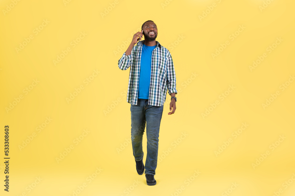 Fototapeta premium African Guy Talking On Phone Communicating Walking Over Yellow Background