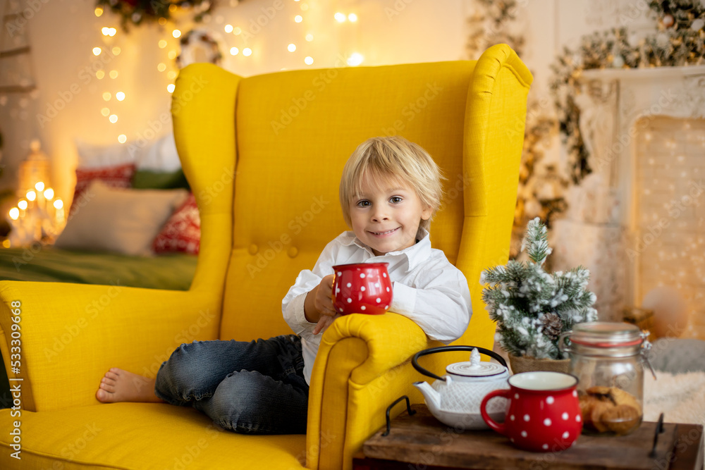 Cute child, boy, sitting on a yellow armchair in a decorated room for Christmas Cute child, boy, sitting on a yellow armchair in a decorated room for Christmas
