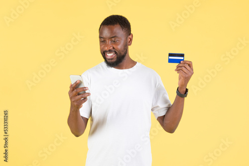 Black Guy Using Smartphone And Credit Card Shopping, Yellow Background