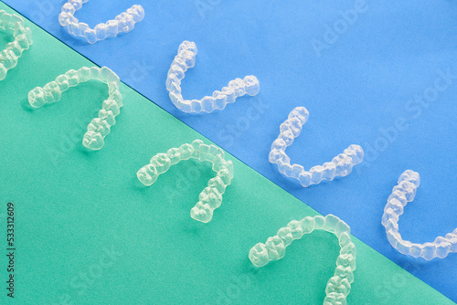  Transparent, invisible dental aligners or braces applicable to orthodontic treatment are placed on a blue and green background.