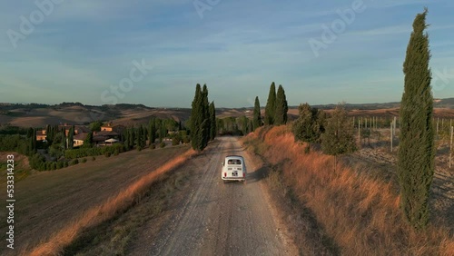 Drone shot of a little Italian vehicle driving a countryside road with trees. Florence, Tuscany, Italy.