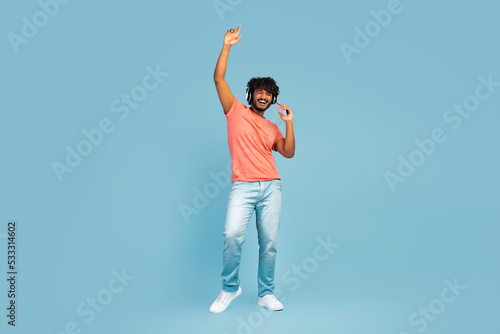 Positive hindu guy listening to music and dancing, using headphones