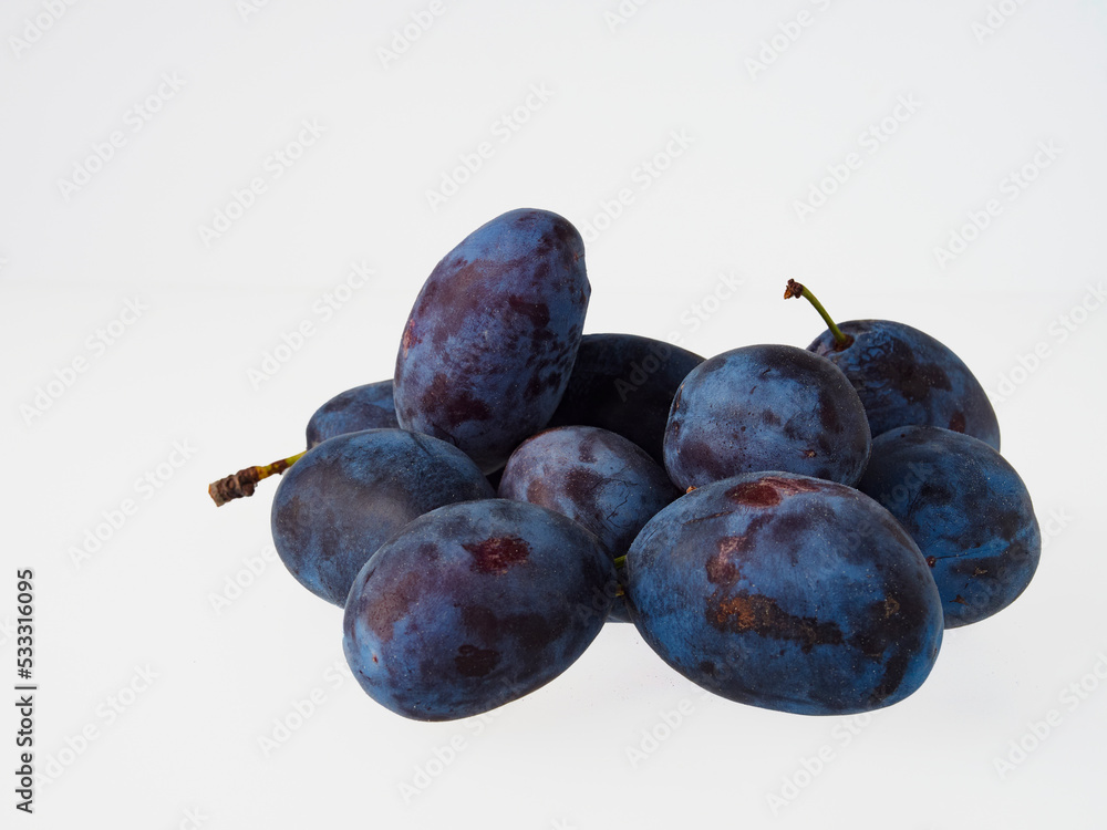 Black plums on wood background. Pile of black plums on a white serving plate. close up
