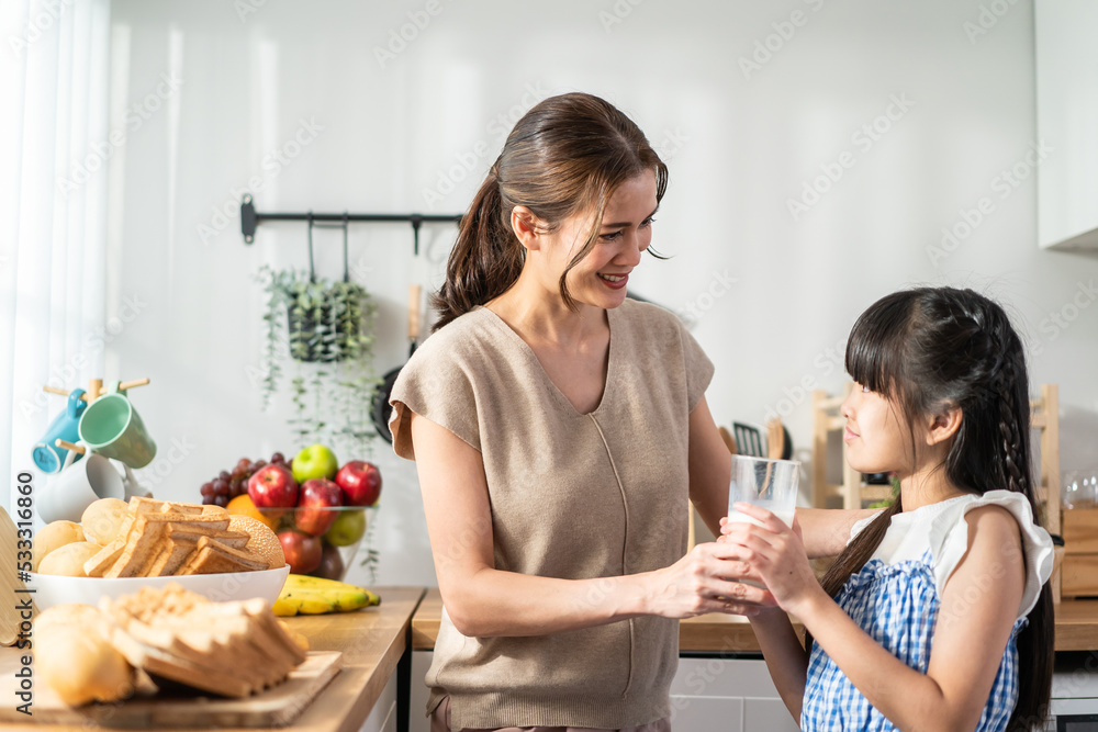 Asian little cute kid holding a cup of milk and drinking with mother. 