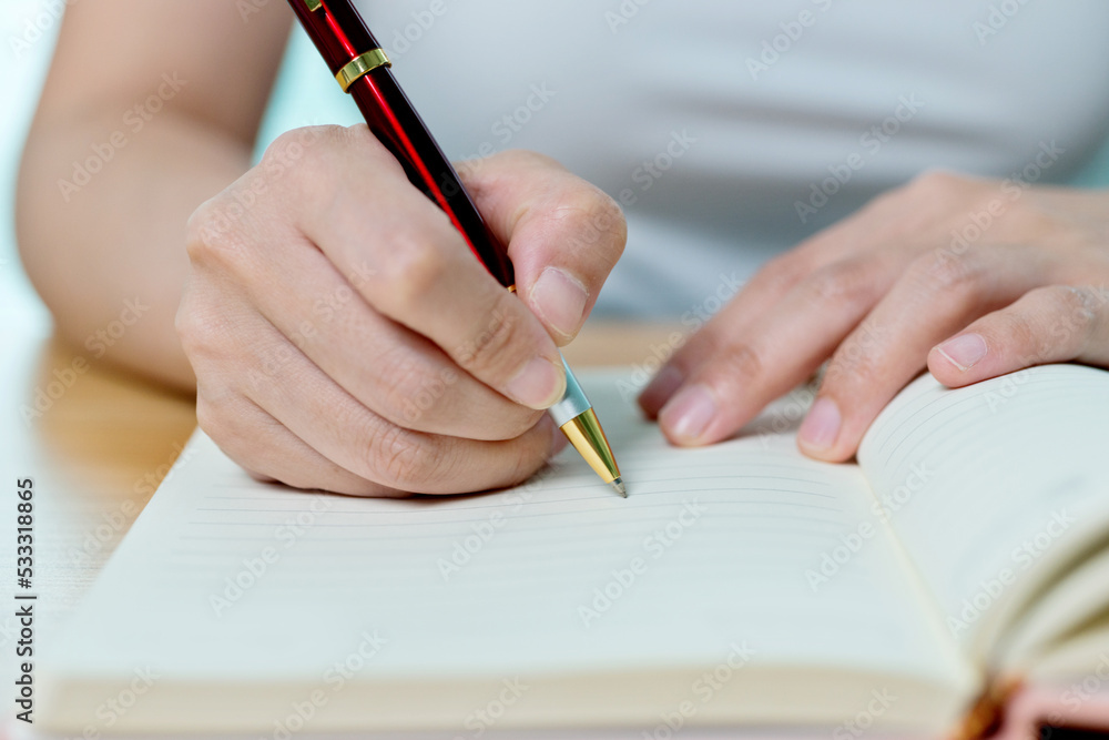 Hands writing in notepad on wooden table Hands writing in notepad on wooden table