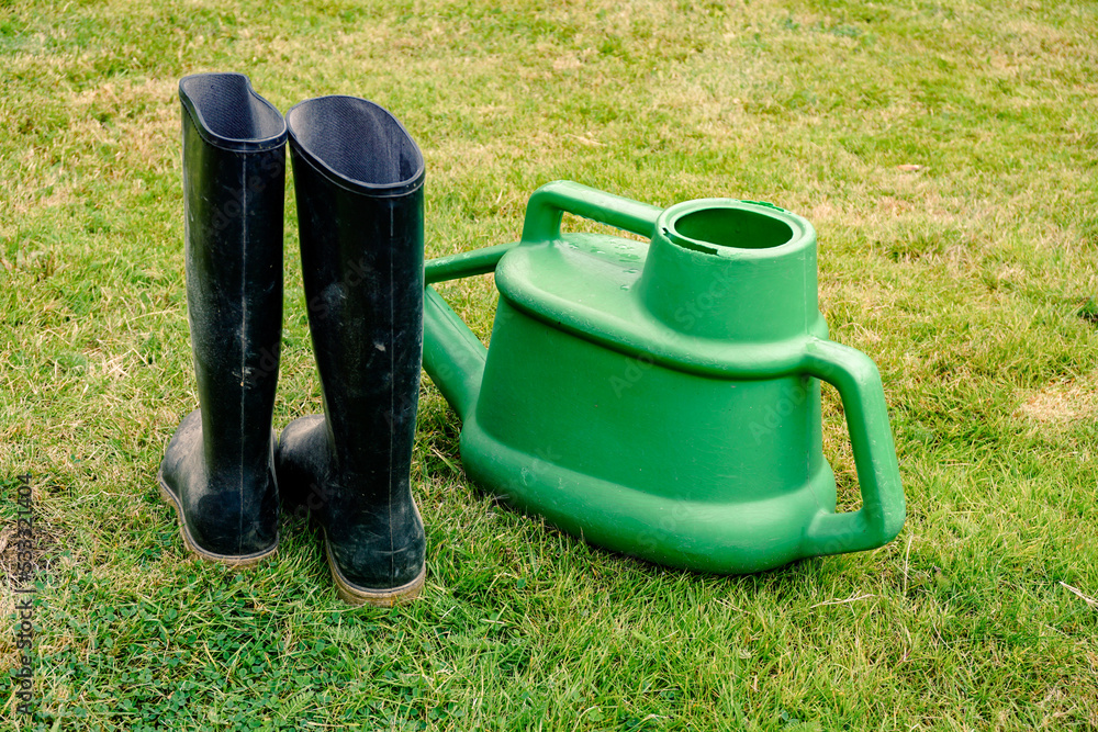 gardening equipment. A pair of wellington boots and plastic watering can on grass lawn. gardening equipment. A pair of wellington boots and plastic watering can on grass lawn.