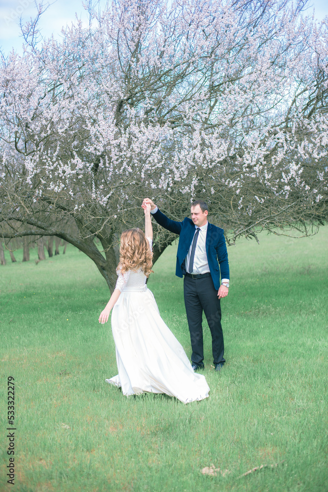The bride and groom with blond long hair in a white dress in a spring garden near a flowering tree. Emotions and feelings The bride and groom with blond long hair in a white dress in a spring garden near a flowering tree. Emotions and feelings