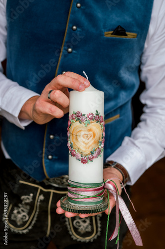 Close up shot of man holding wedding candle in hands in traditional Bavarian clothes