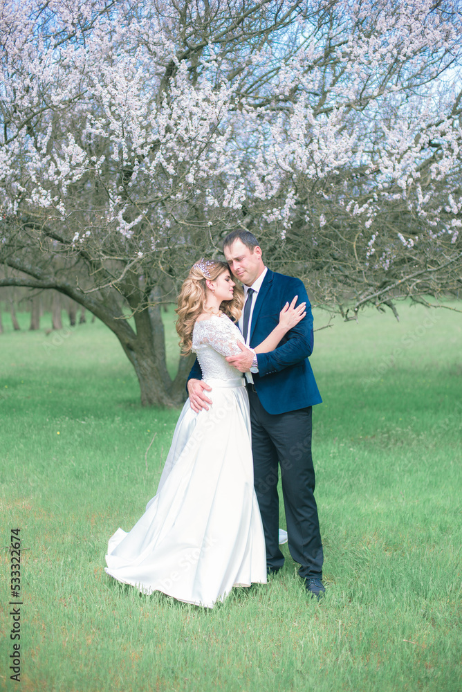 The bride and groom with blond long hair in a white dress in a spring garden near a flowering tree. Emotions and feelings