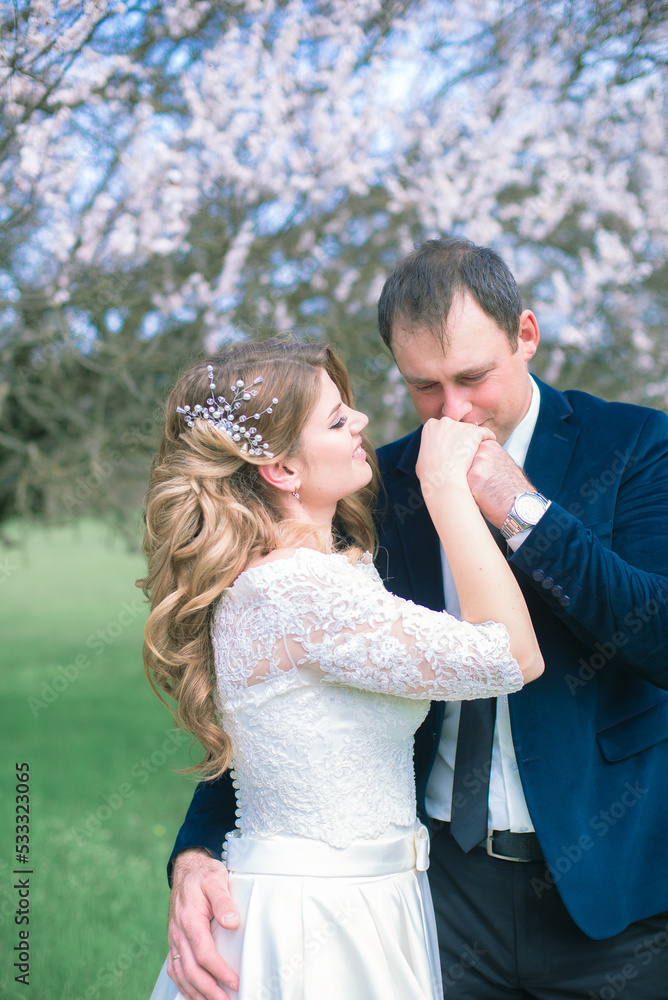 The bride and groom with blond long hair in a white dress in a spring garden near a flowering tree. Emotions and feelings The bride and groom with blond long hair in a white dress in a spring garden near a flowering tree. Emotions and feelings