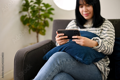 A woman using her mobile phone, watching something on internet while relaxing in living room.
