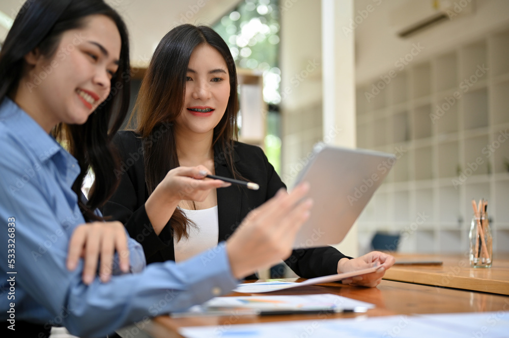 Two cheerful young Asian marketing workers are looking at a video on tablet screen Two cheerful young Asian marketing workers are looking at a video on tablet screen