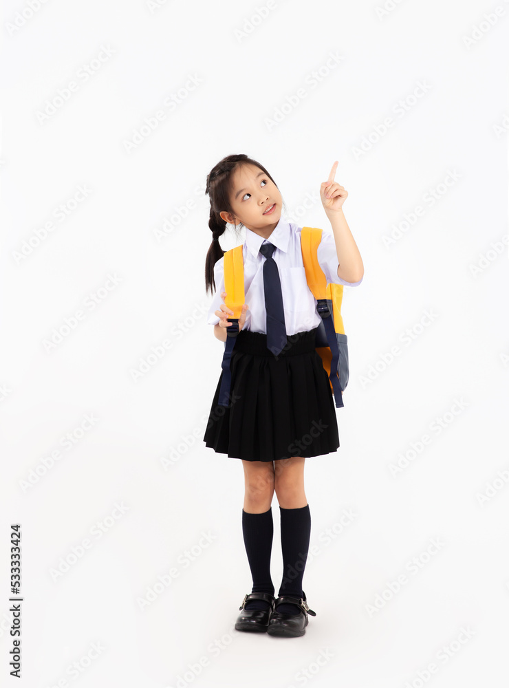 Back to school concept. Cute asian junior school student kid in uniform with yellow backpack posing finger pointing on white background. Back to school concept. Cute asian junior school student kid in uniform with yellow backpack posing finger pointing on white background.