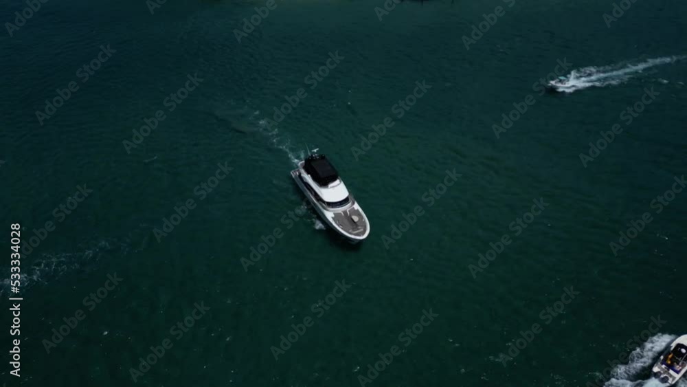 A Luxury Yacht Moving Slowly Navigating Between Smaller Boats on a River from an Aerial Drone Perspective Looking Down on the Water Below. A Luxury Yacht Moving Slowly Navigating Between Smaller Boats on a River from an Aerial Drone Perspective Looking Down on the Water Below.