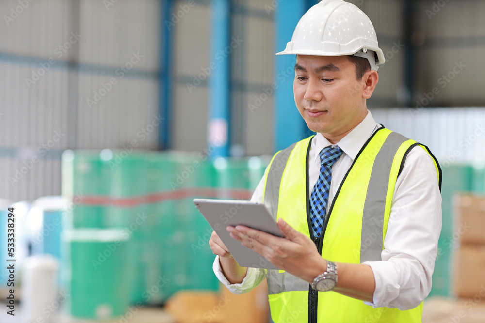 Architect or engineering man and worker standing and checking large warehouse with tablet. Asian business manager looking in future with warehouse building background. Architect or engineering man and worker standing and checking large warehouse with tablet. Asian business manager looking in future with warehouse building background.