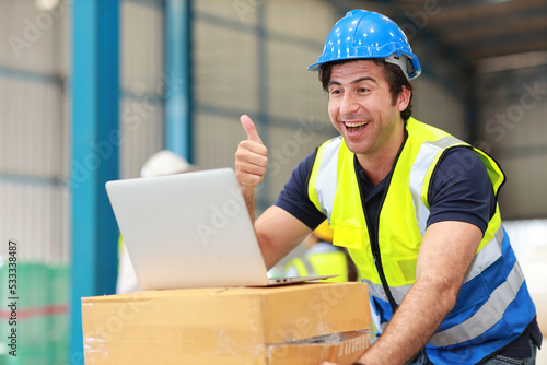 Architect or engineering man and worker standing and checking large warehouse with computer. Caucasian business manager showing thumb up with warehouse building background.