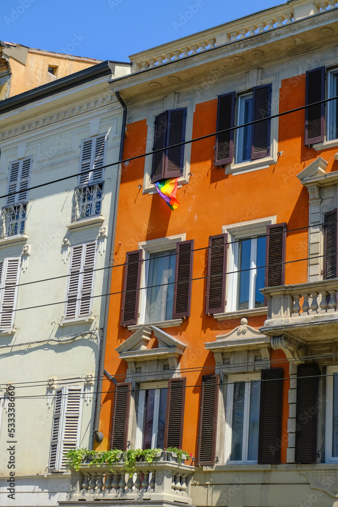 Naklejka premium facade of an orange house in the old town of Parma, Italy with Rainbow banners, and flags. LGBTQ+ banner