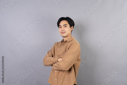 nice positive asian man smiling with folded arms wearing classic shirt holding hands crossed. isolated on a gray background. proud with his Achievement.