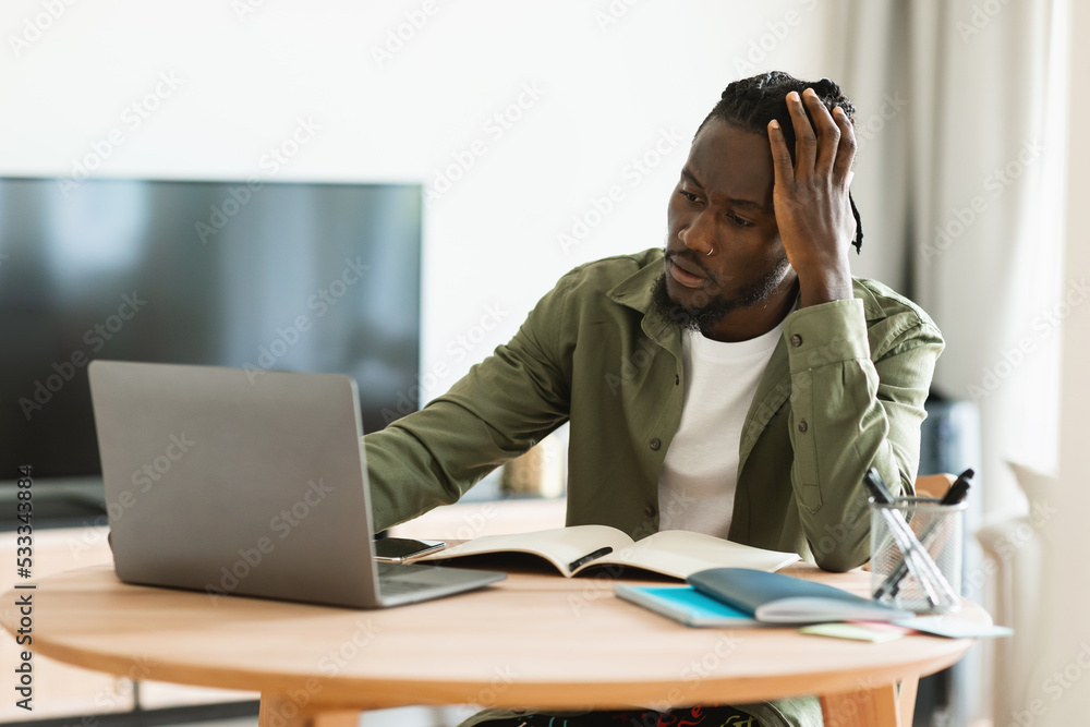 Thoughtful black man using laptop computer working online and thinking about business, sitting at home office Thoughtful black man using laptop computer working online and thinking about business, sitting at home office