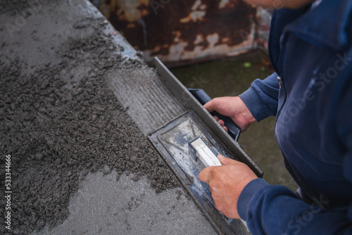 A close up of worker hands putting a concrete on the ground and spreading it with tools