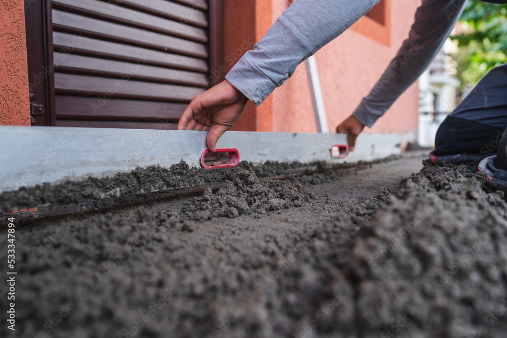 A close up of worker hands putting a concrete on the ground and spreading it with tools A close up of worker hands putting a concrete on the ground and spreading it with tools