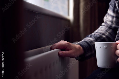 Close Up Of Mature Man Trying To Keep Warm By Radiator At Home During Cost Of Living Energy Crisis photo