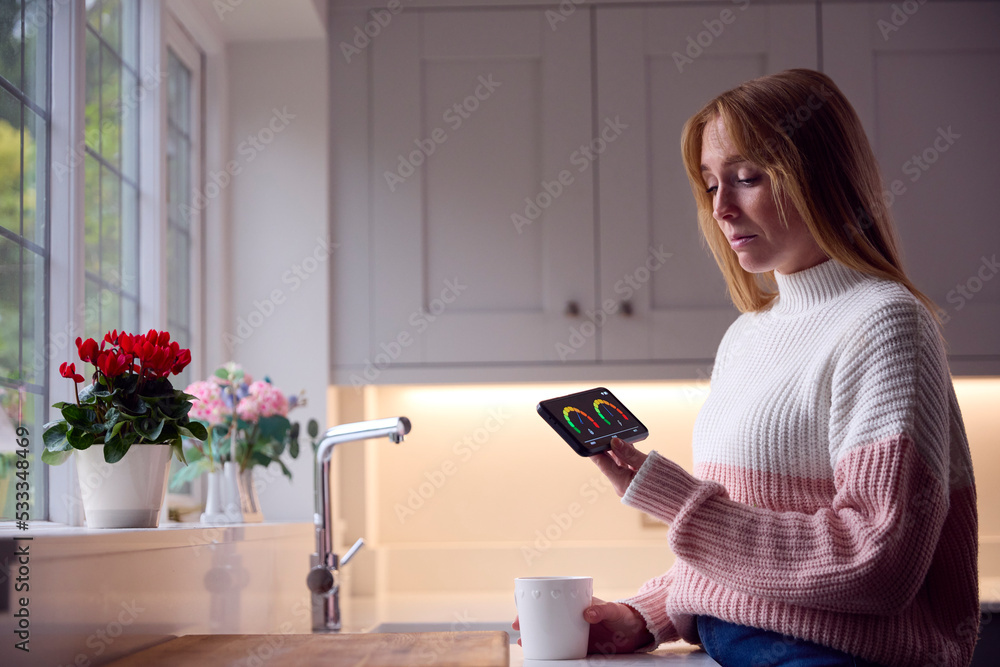Worried Woman Looking At Smart Meter In Kitchen At Home During Cost Of Living Energy Crisis Worried Woman Looking At Smart Meter In Kitchen At Home During Cost Of Living Energy Crisis