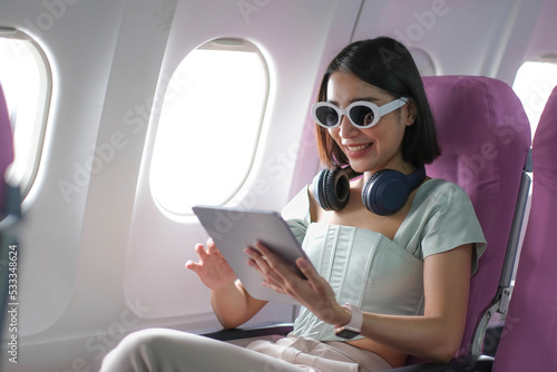 Travel tourism with modern technology and air flights concept, woman sitting in plane with modern digital gadget and searching favourite music playlist in application for listening