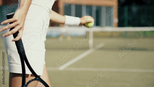 4k video Unrecognizable young woman in white on tennis grass court bouncing the ball before serving. Female playing tennis on sunny day. Tennis club concept.
