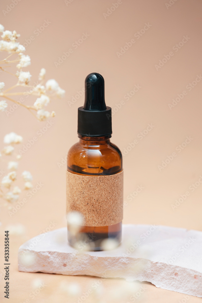 Amber glass dropper bottles with craft label filled serum or essential oil. Beige background with daylight with beautiful flowers.