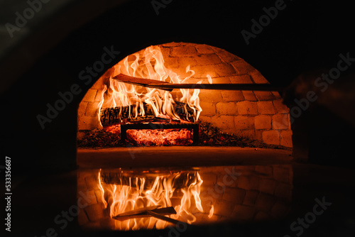 A traditional oven for cooking and baking pizza with a shovel. Firewood burning in the oven. Wood-fired oven. Image of a brick pizza oven with fire. photo
