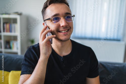 A young man working on laptop and talking on the phone about business from his home office during the day
