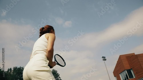 4k video female tennis player in white serving. Young woman hit the tennis ball with racket. Tennis serve on sky background.